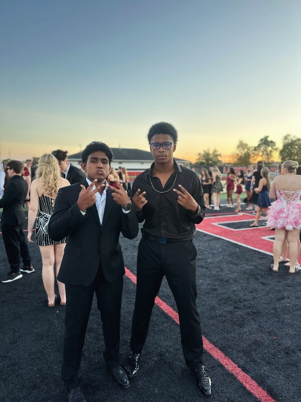 Two young men in formal wear posing on a sports field at sunset.