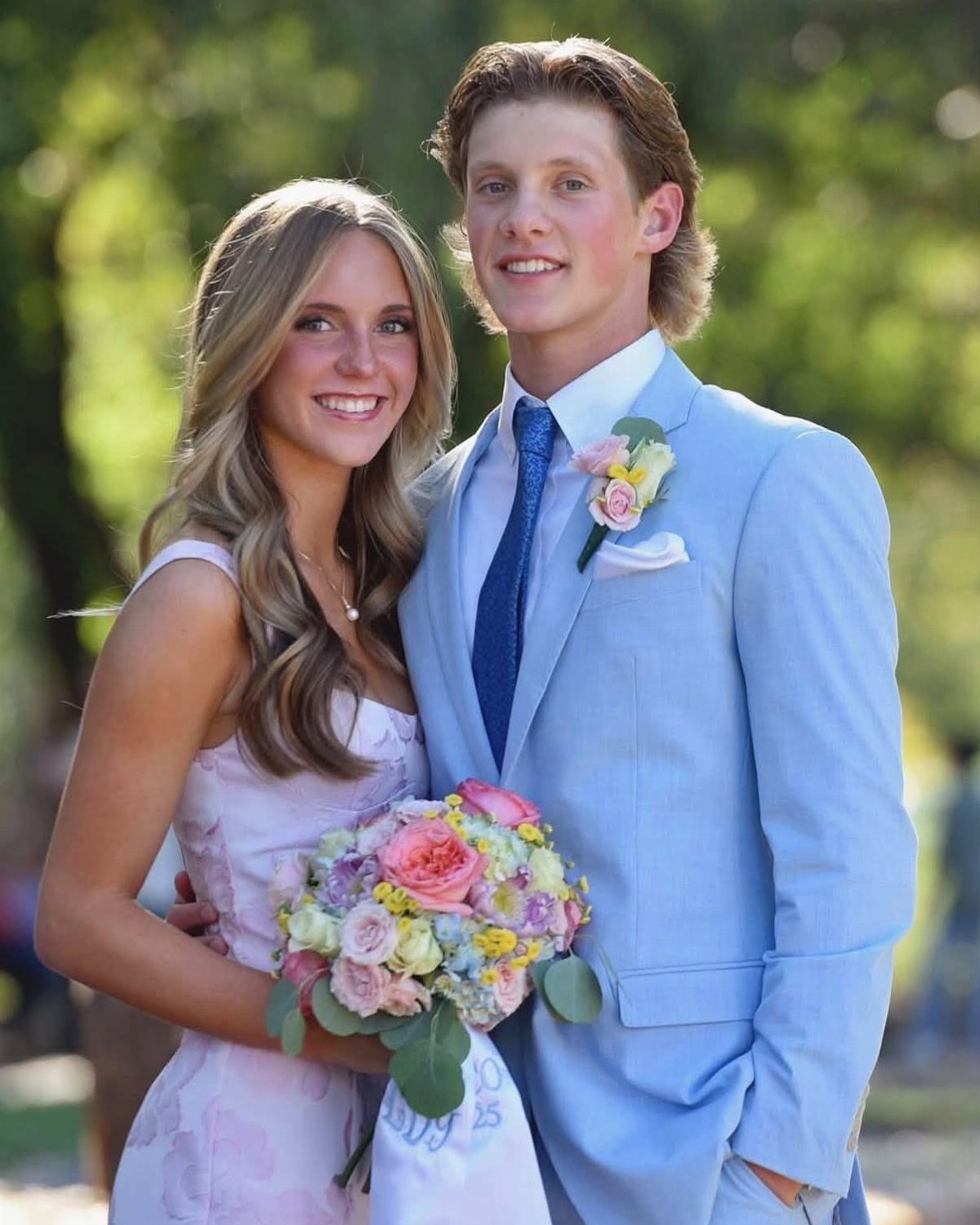 Young couple in formal attire posing together with a colorful floral bouquet.