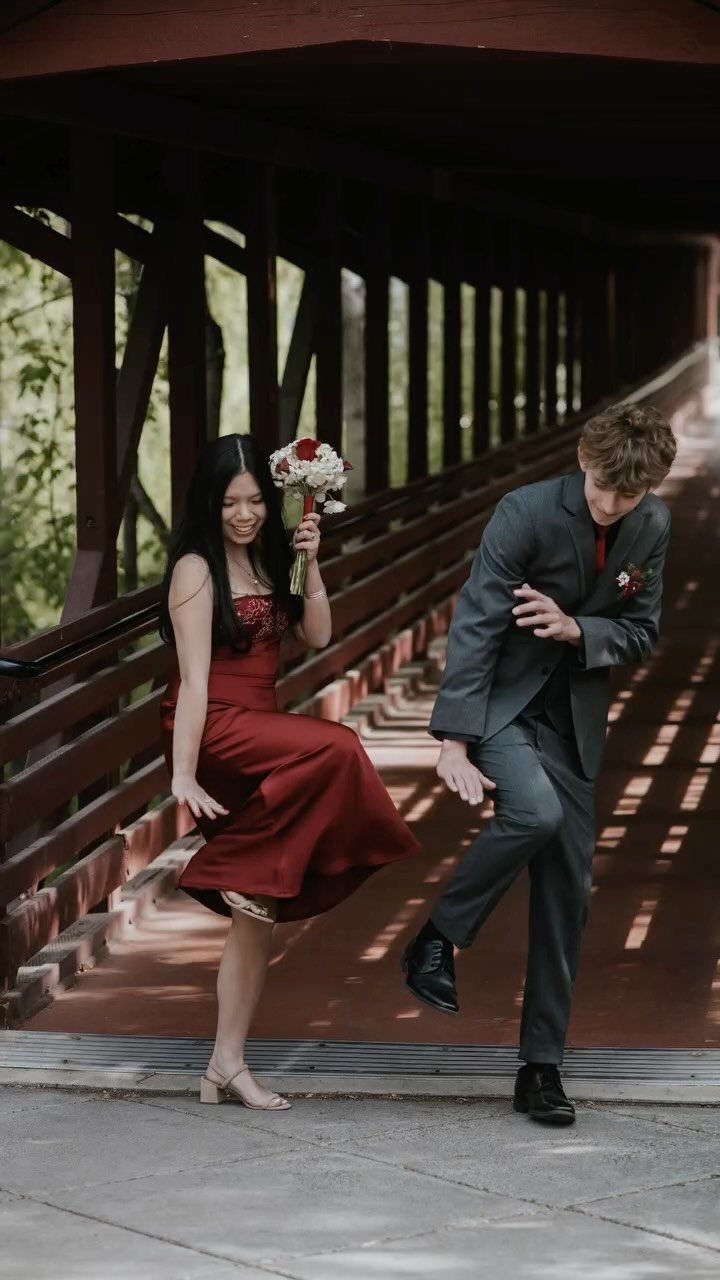Couple in formal wear dancing on a wooden bridge with a red bouquet.