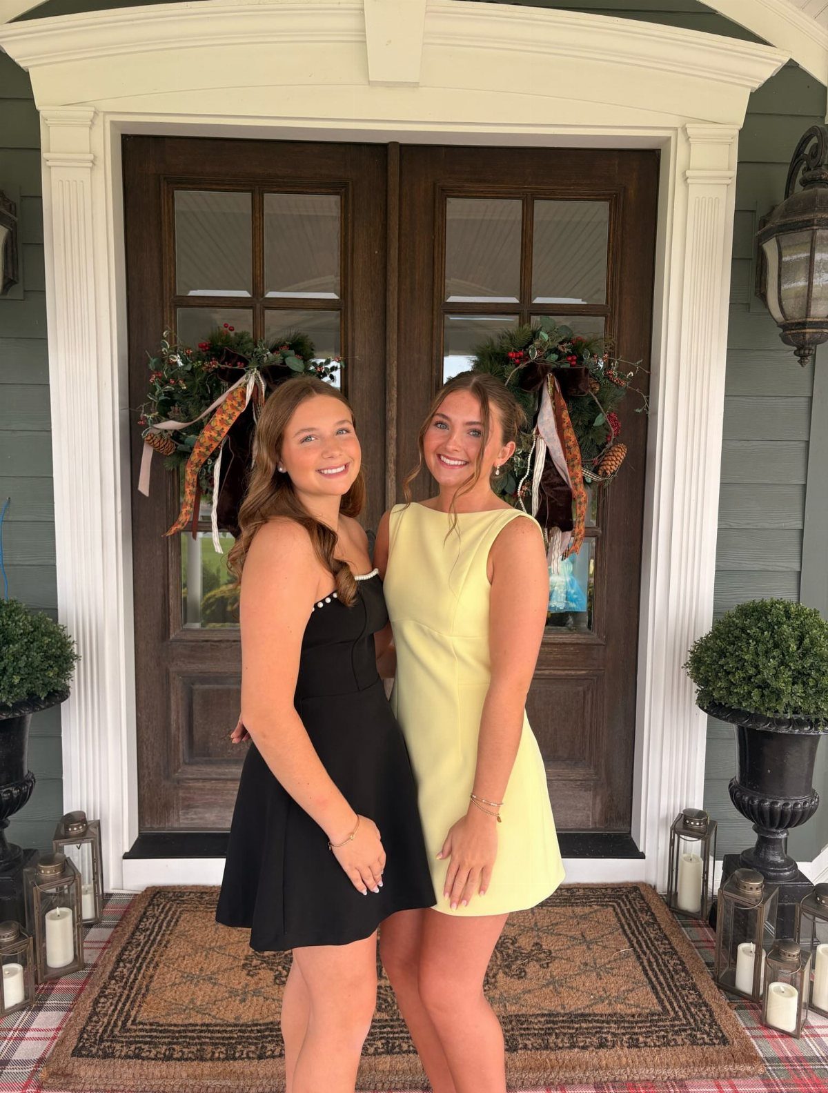Two teenage girls in cocktail dresses posing on a porch for homecoming photos.