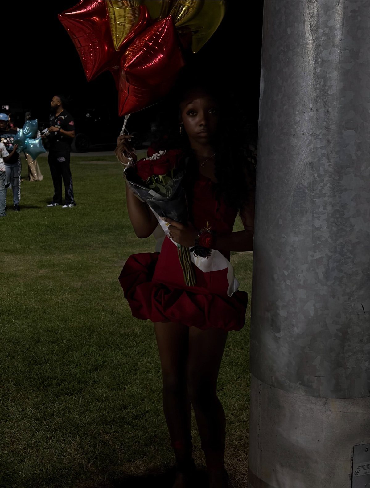 Young woman in red dress holding roses and star balloons outdoors at night