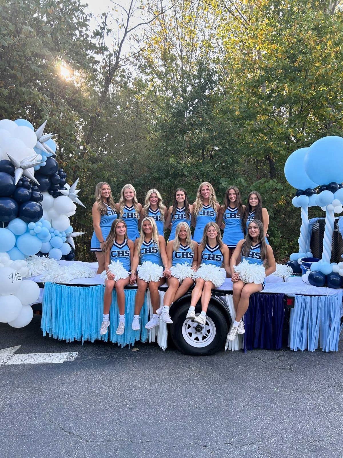 Cheerleaders in blue uniforms posing on a decorated homecoming float with balloons.