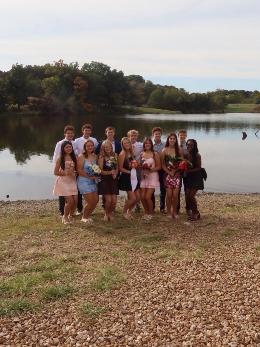 Teenagers in formal attire posing for a group photo by a lake shore.