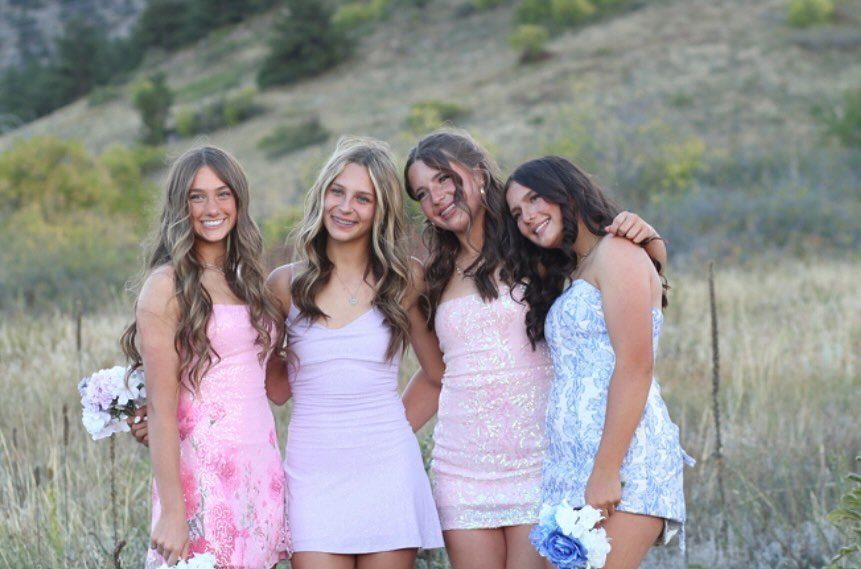 Four teenage girls in colorful dresses posing and smiling in a grassy field.