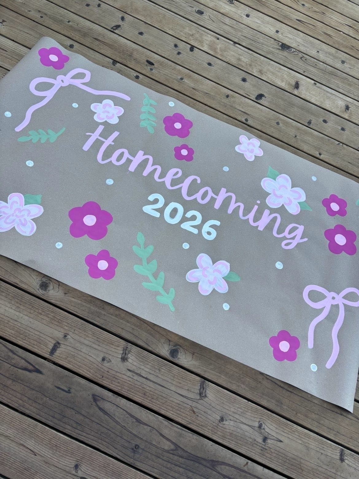 Brown paper homecoming poster with floral decorations and 2026 text on wooden decking