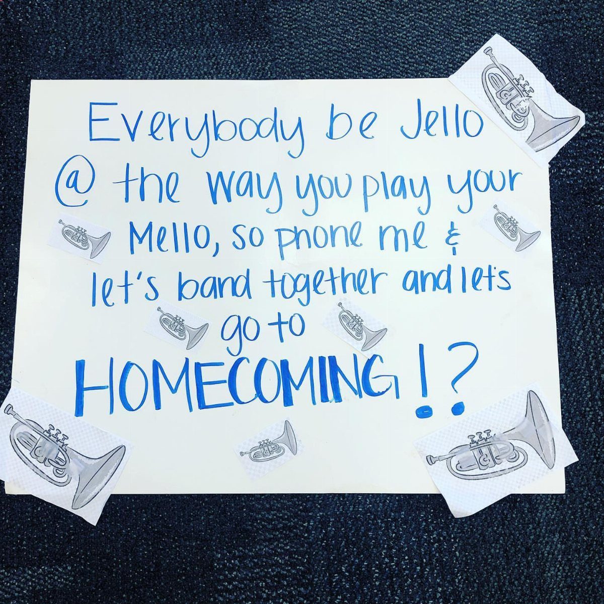 Handwritten homecoming proposal sign with blue text and trumpet drawings on white paper.