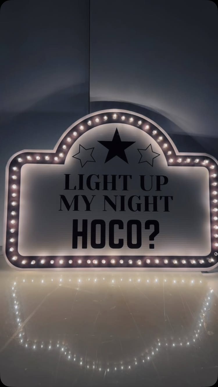 Marquee sign with lights reading Light Up My Night HOCO? on reflective floor