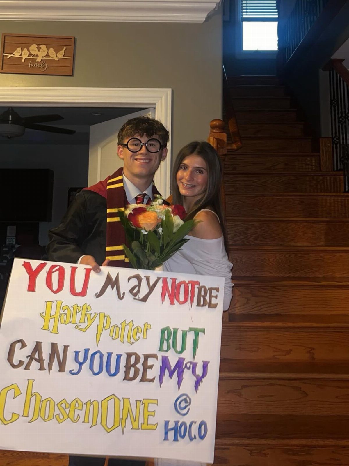 Teenage boy in Harry Potter costume holding a homecoming proposal sign and a girl.