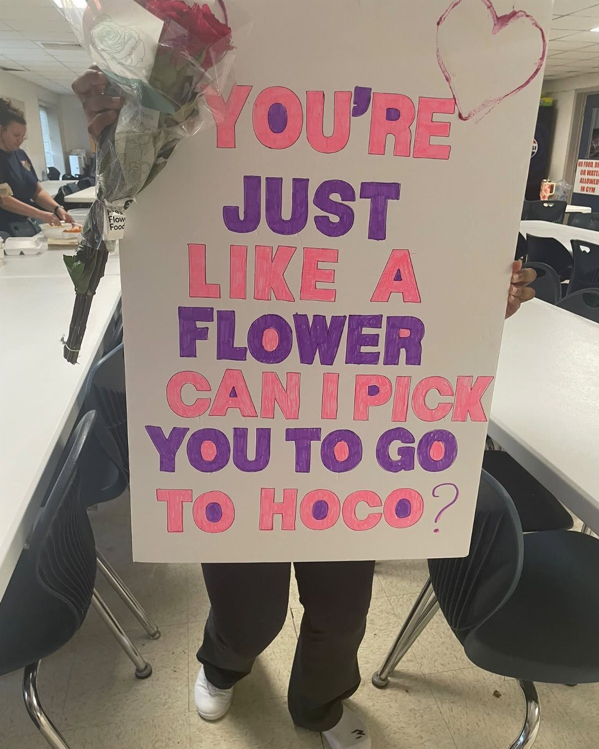 White homecoming proposal sign with flower puns and a bouquet of red roses