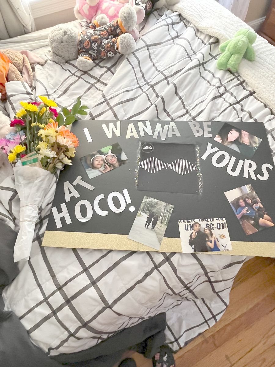 Black homecoming proposal sign with photos and flowers on a white grid bedsheet
