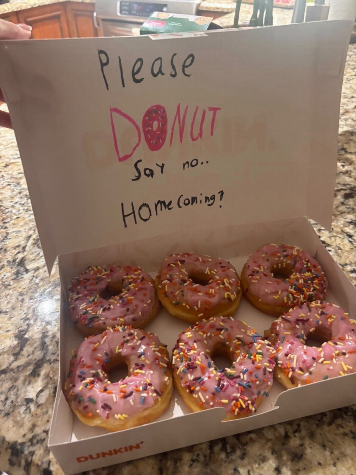Open donut box with a handwritten homecoming proposal message on the inside lid.