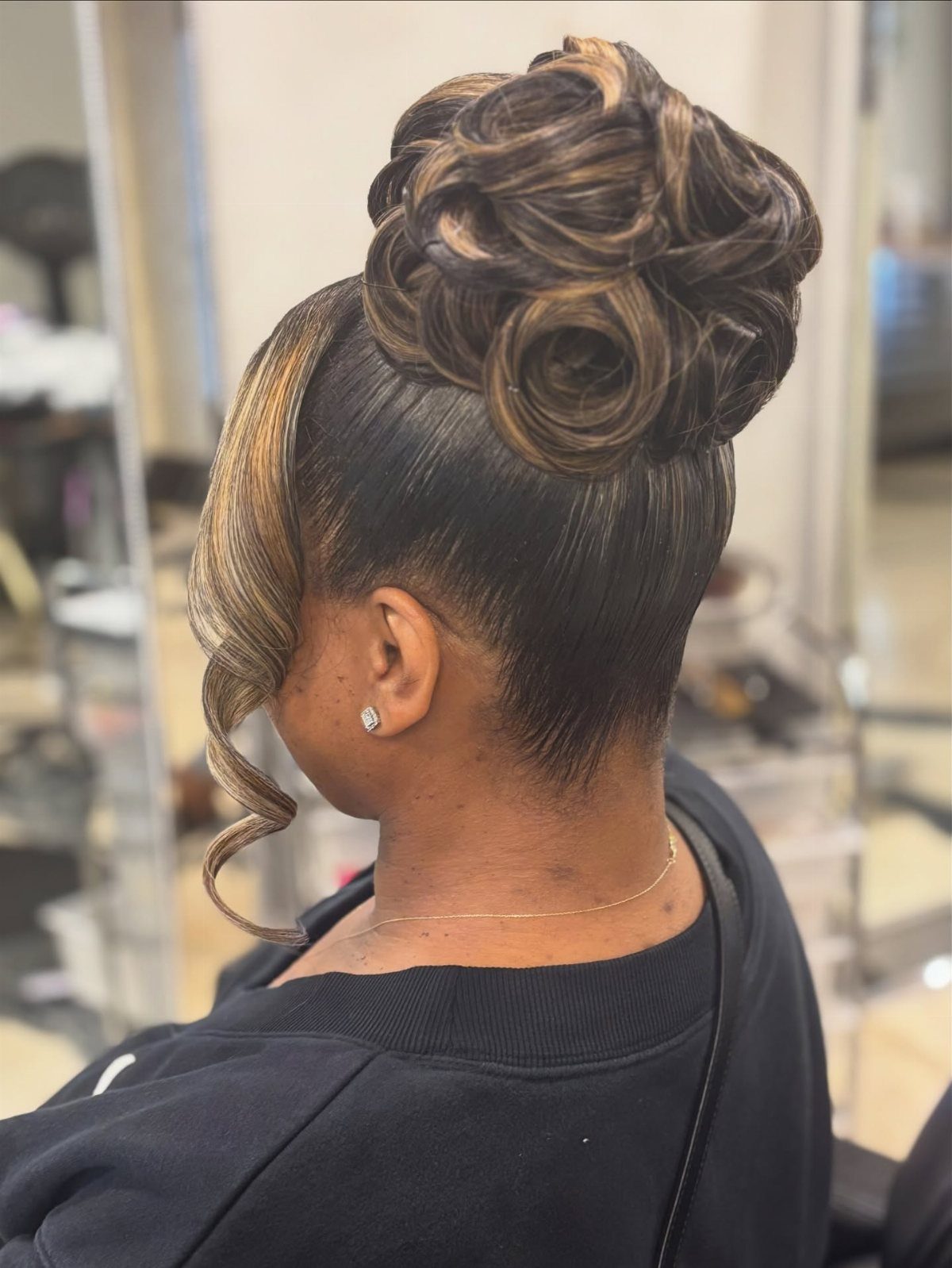 High voluminous curly updo with blonde highlights and a face-framing curl.
