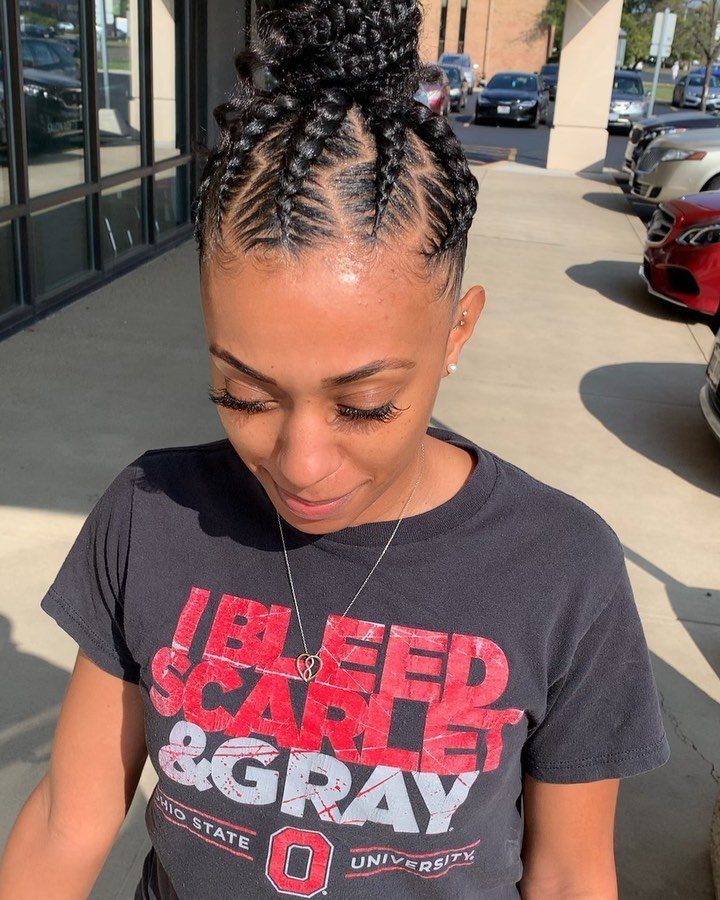 Woman with braided cornrows styled into a high bun wearing a black t-shirt.