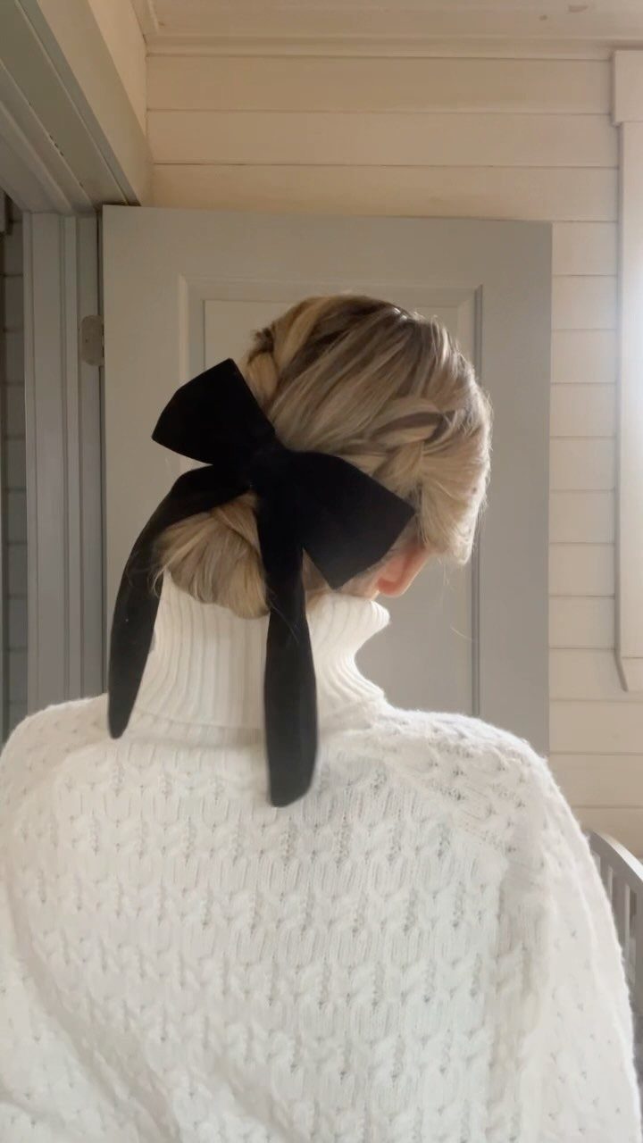 Blonde braided updo hairstyle with a large black velvet bow and white sweater.