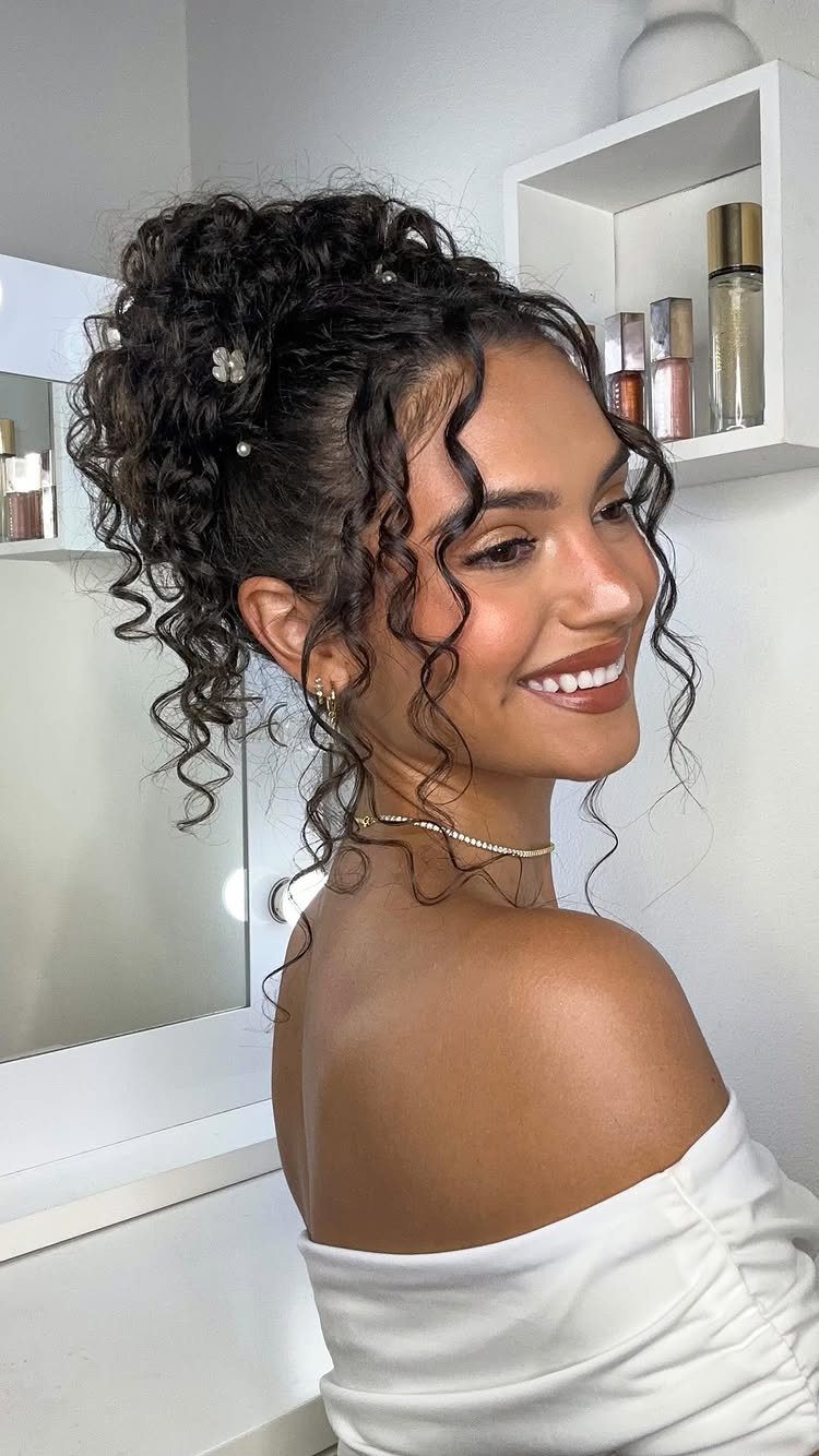 Woman with curly high updo and white floral hair accessories smiling in a room