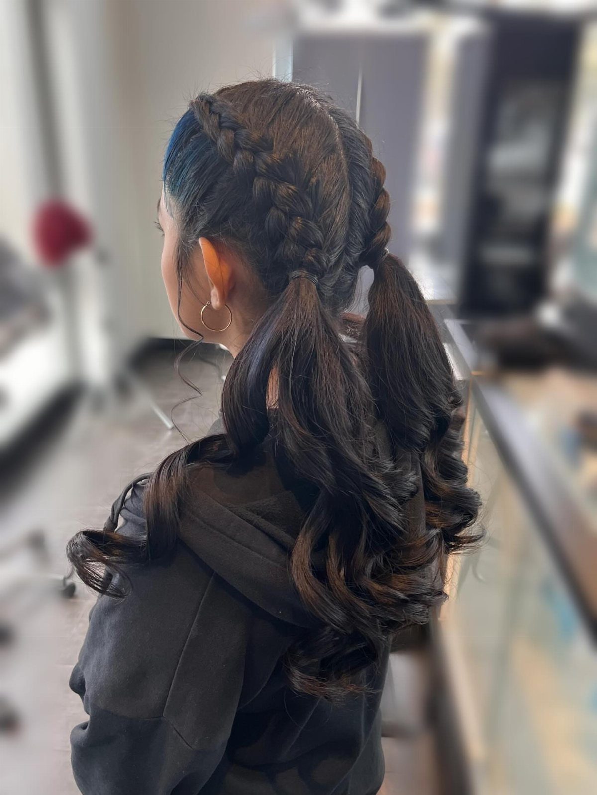 Dark brown hair styled in Dutch braid pigtails with curly ends.