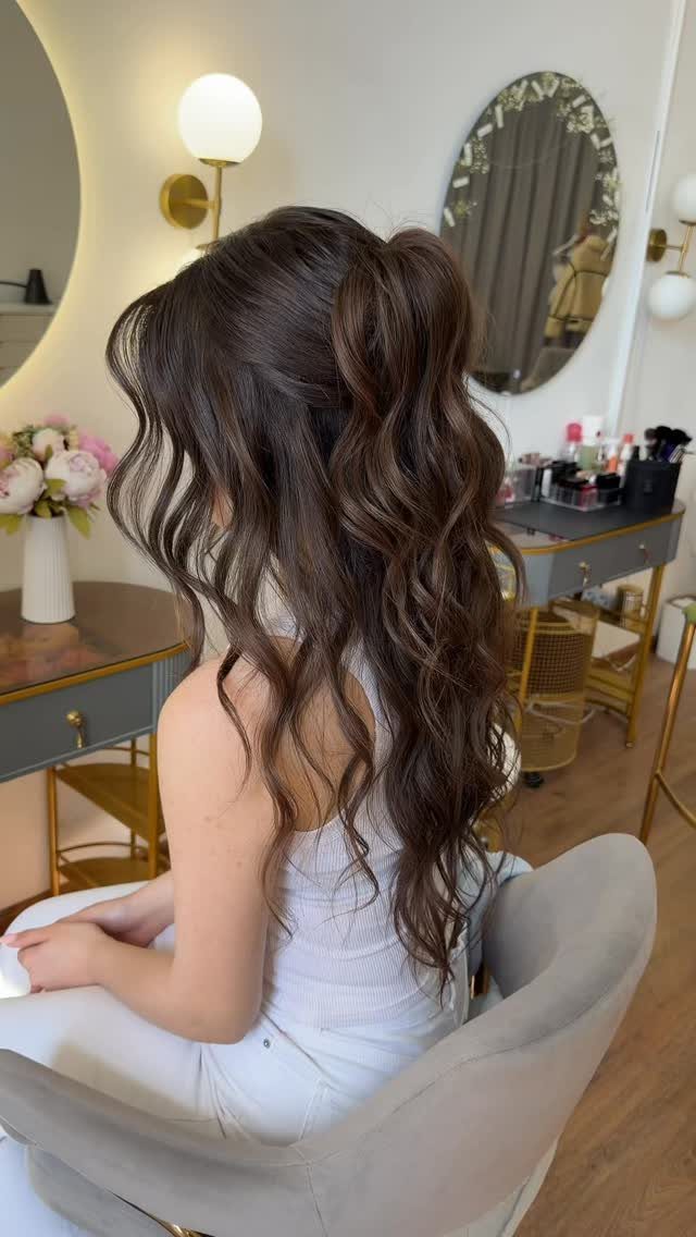 Woman with long brown wavy hair in a half-up half-down hairstyle in a salon.