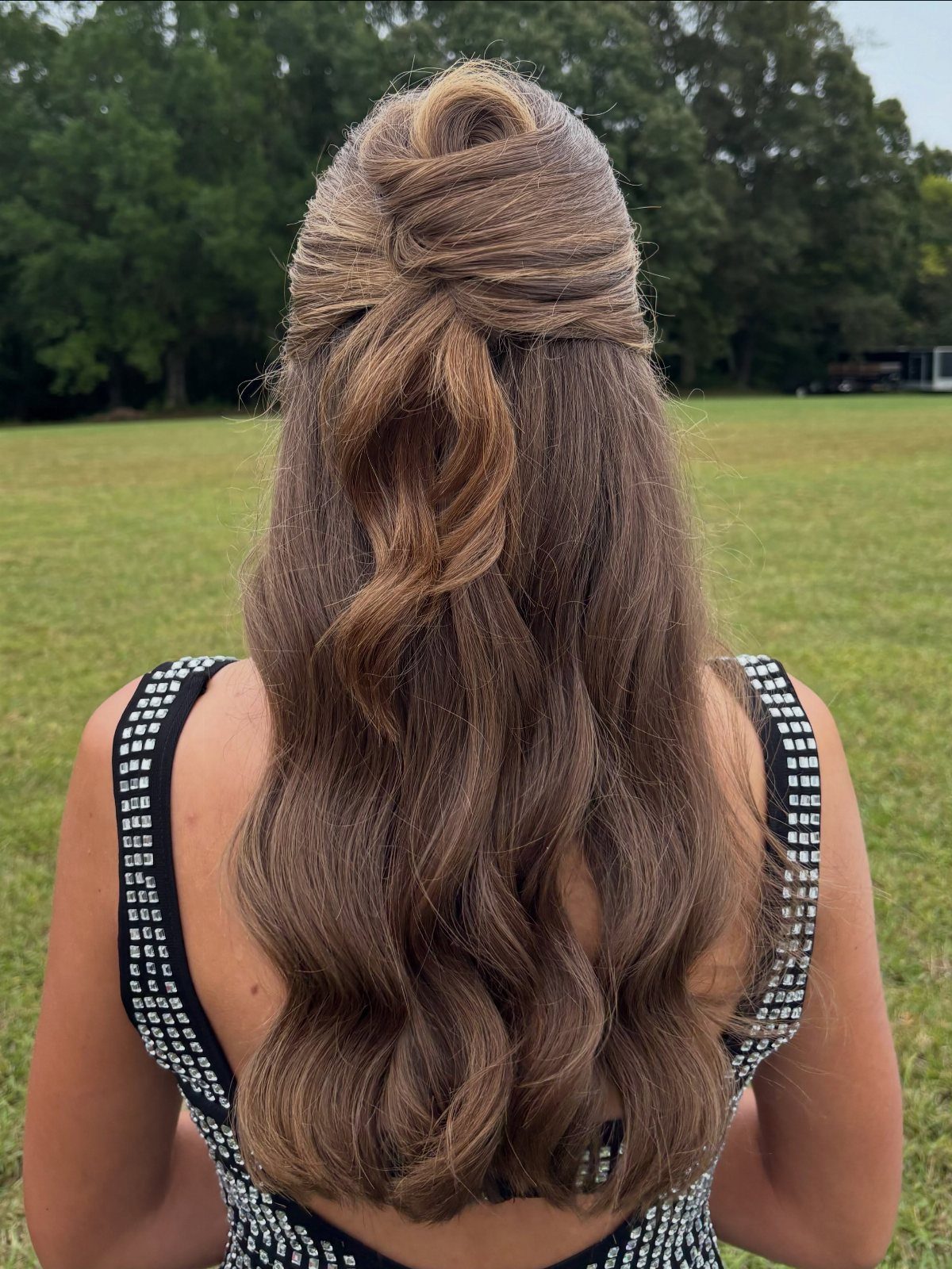 Half-up twist hairstyle with loose brown waves on a person in a formal dress.