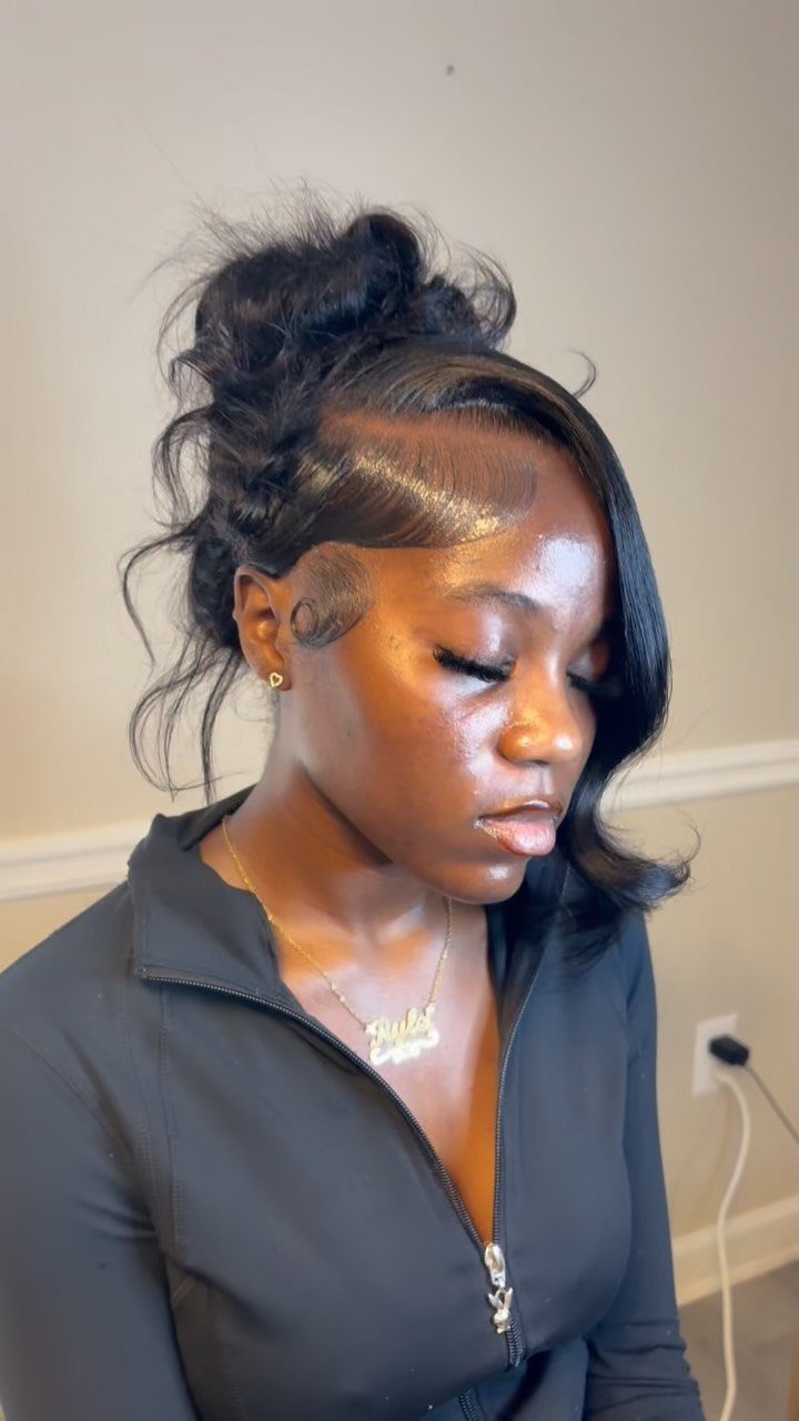 Woman with a high voluminous updo hairstyle and sculpted edges wearing black clothing.