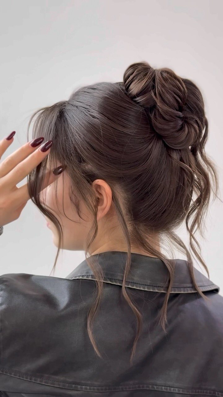 Woman with a high twisted updo and loose curls wearing a leather jacket.