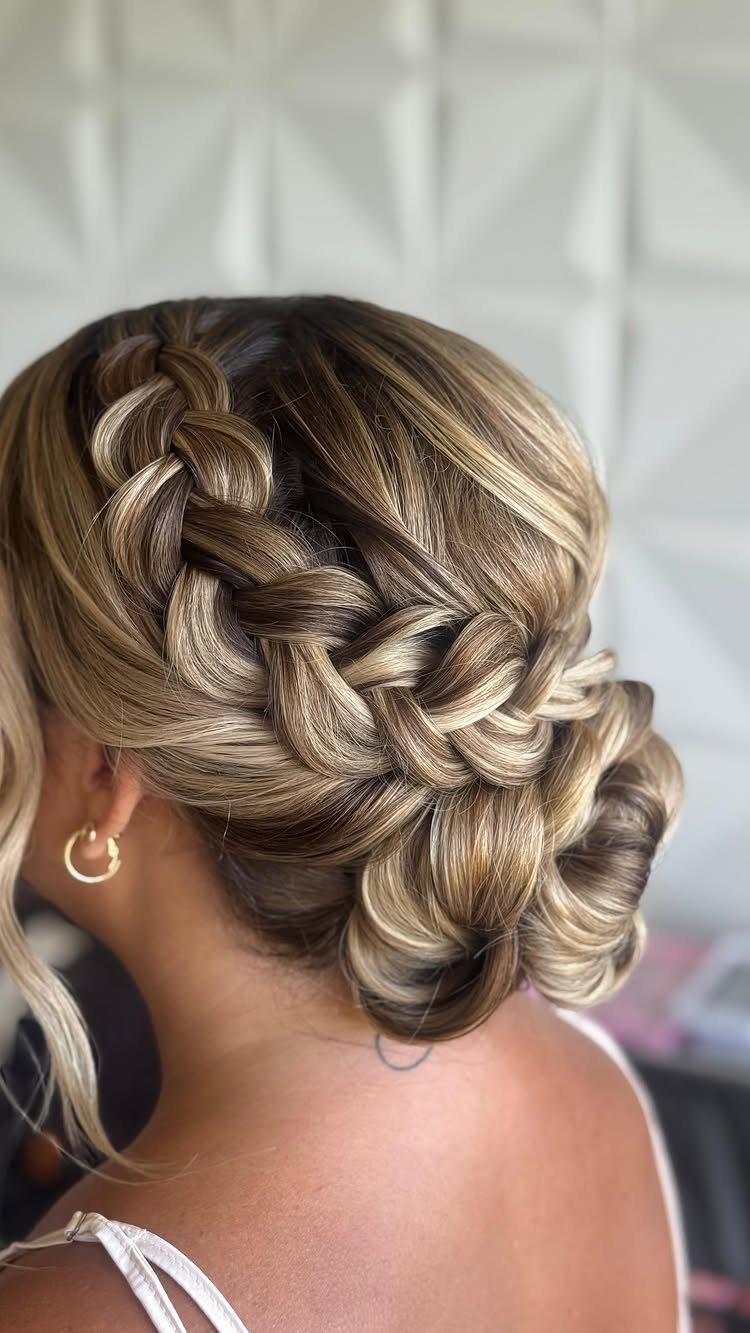 Blonde highlighted hair styled in a side braid ending in a low bun.