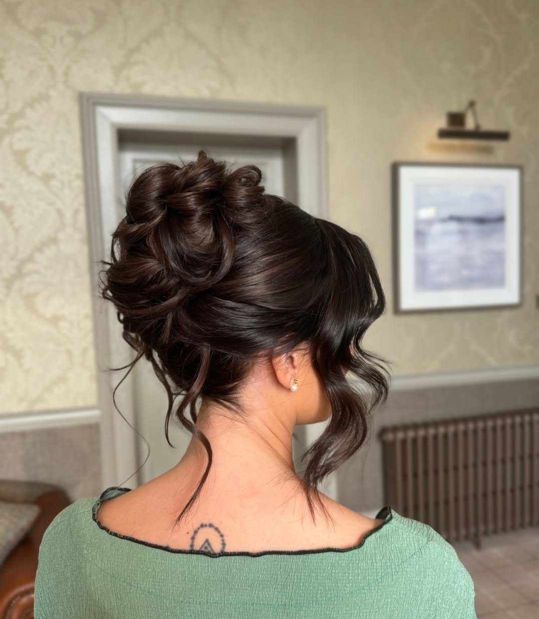 Dark brown voluminous messy bun updo with loose curls framing the neck