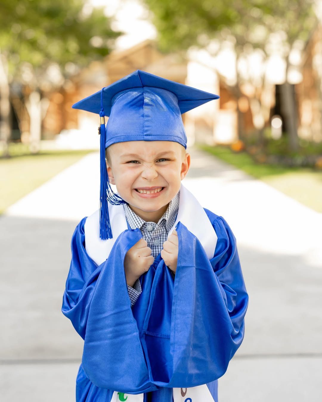 Young boy in blue graduation cap and gown making a funny, excited face.