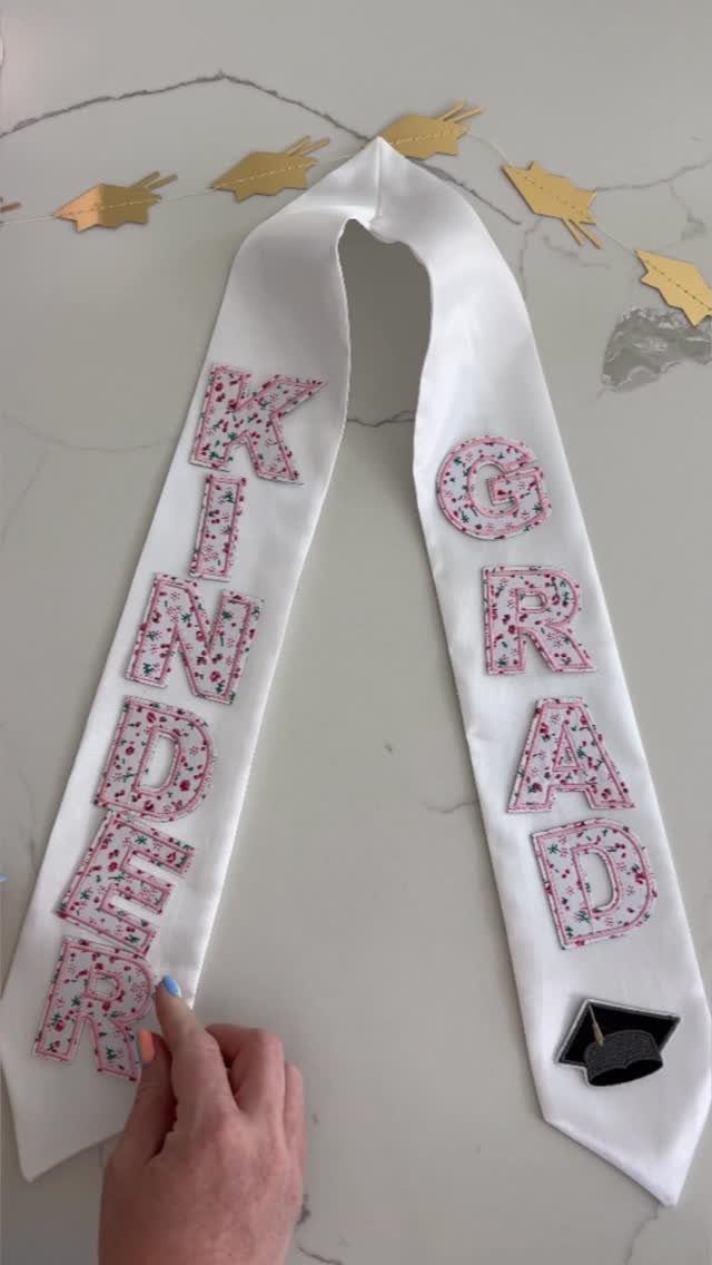 White graduation stole with pink floral Kinder Grad lettering on marble surface