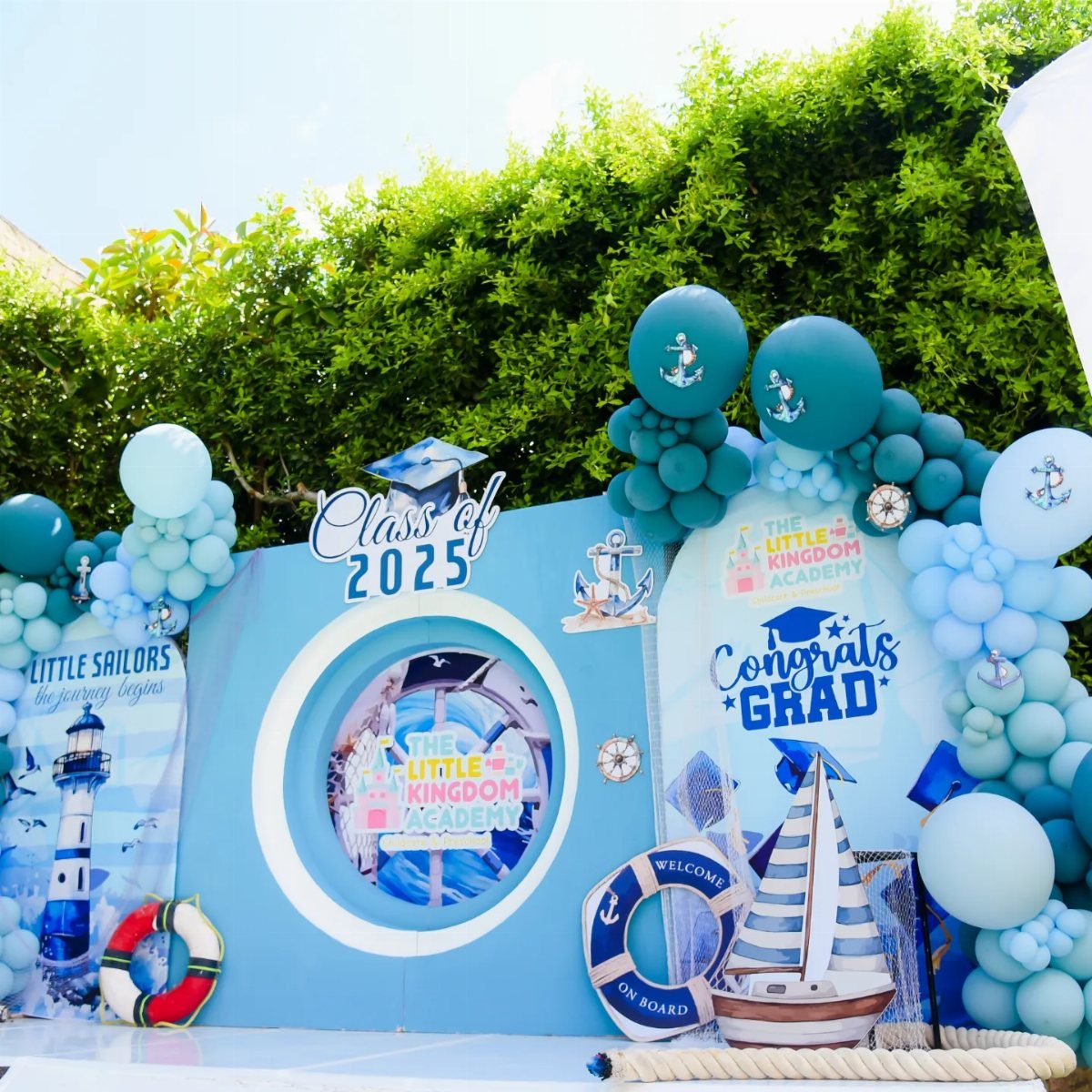 Nautical graduation backdrop with blue balloons, sailboat, and Class of 2025 sign.