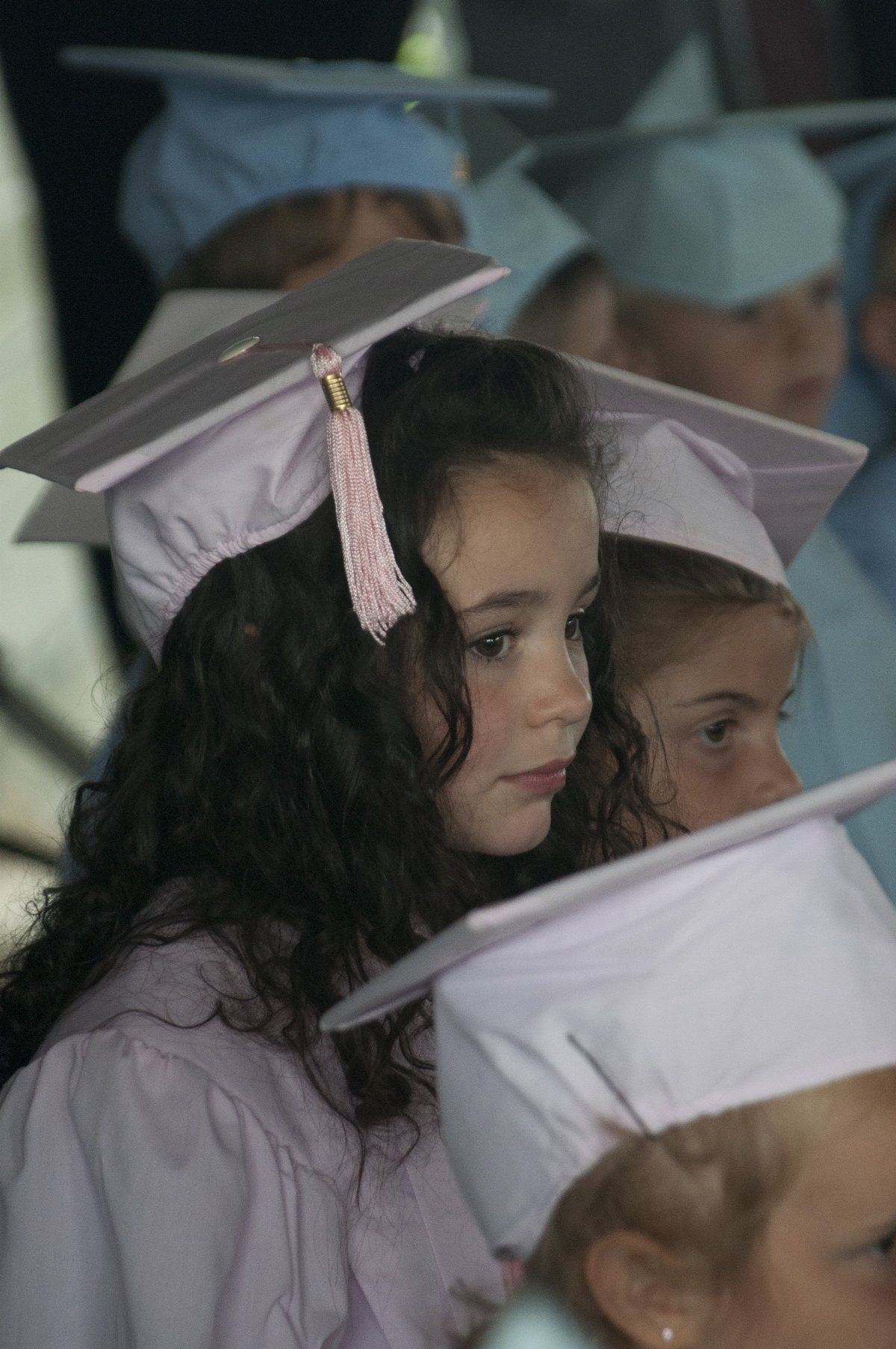 Young girl in purple graduation cap and gown looking thoughtfully off-camera.
