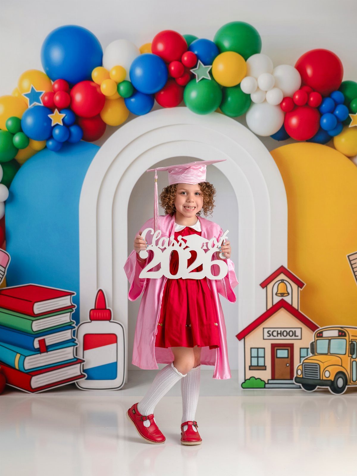 Young girl in pink graduation cap and gown holding a Class of 2026 sign.