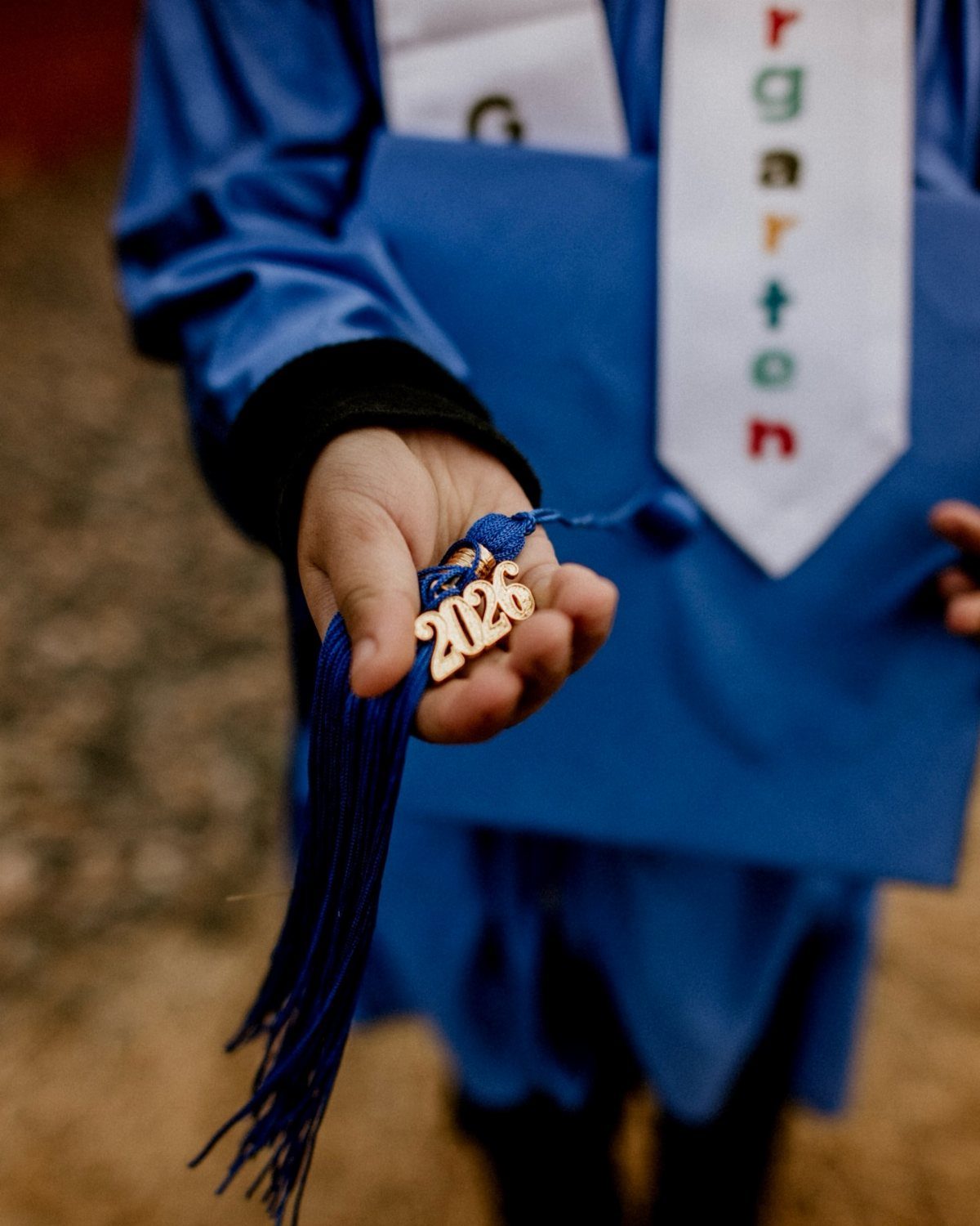 Child's hand holding a blue graduation tassel with a gold 2026 charm