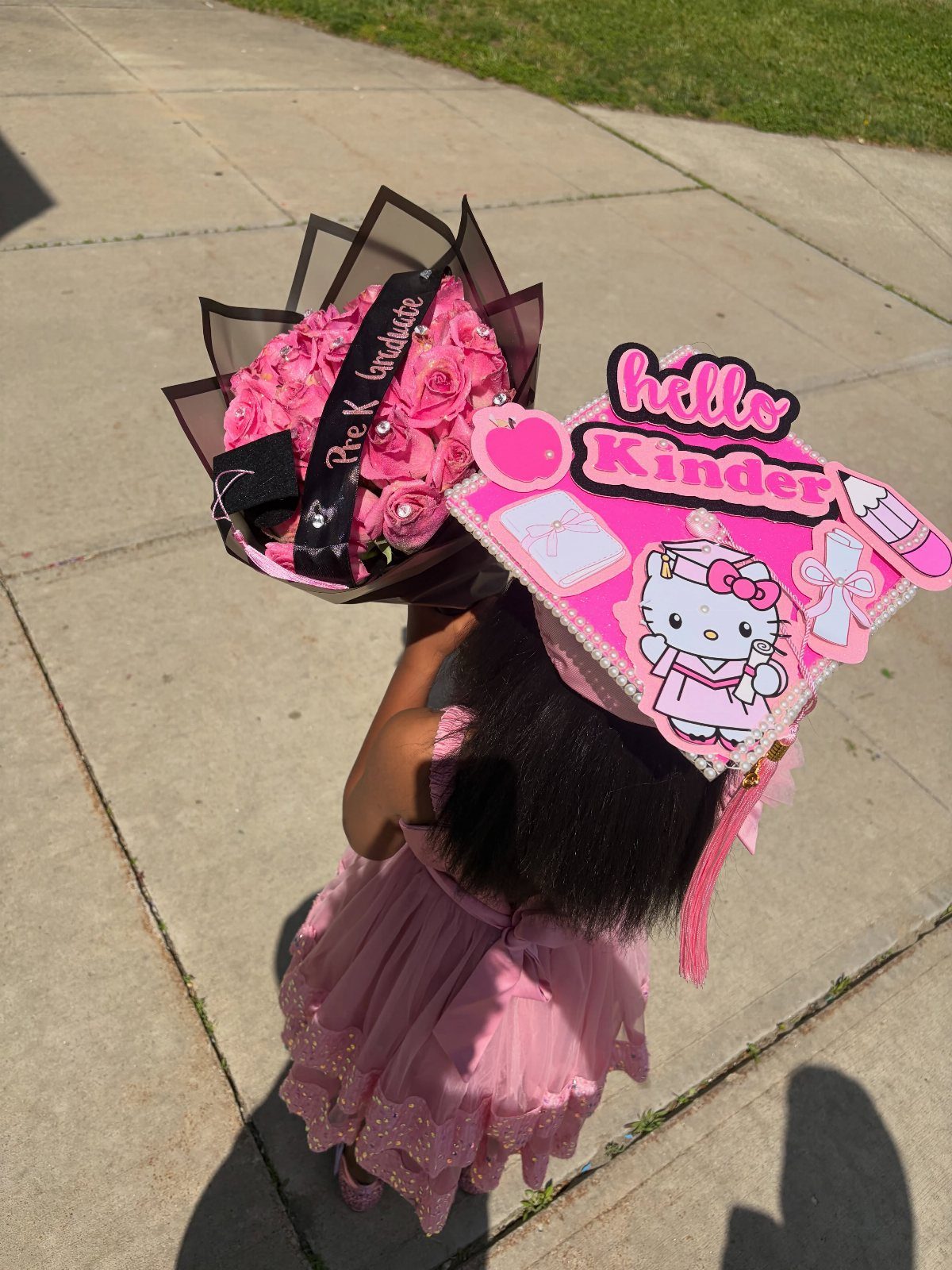 Girl in pink dress wearing a decorated graduation cap holding pink roses.