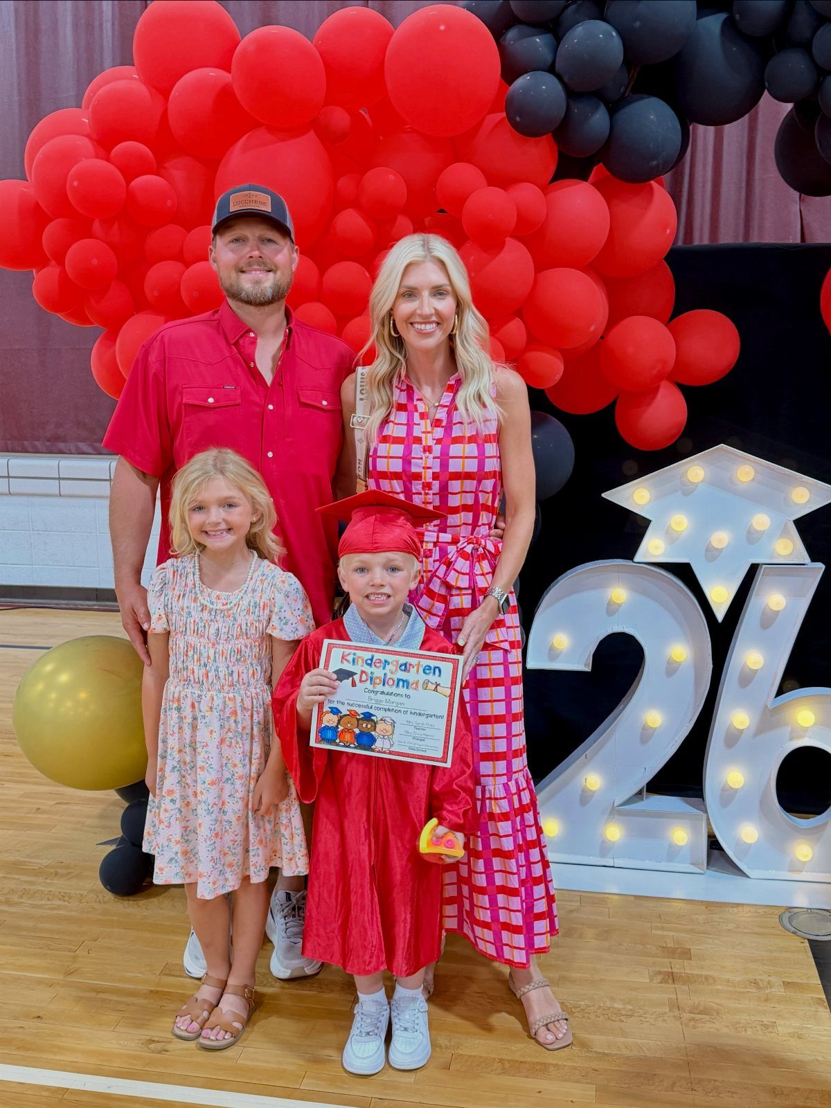 Family posing with a young boy wearing a red kindergarten graduation cap and gown.