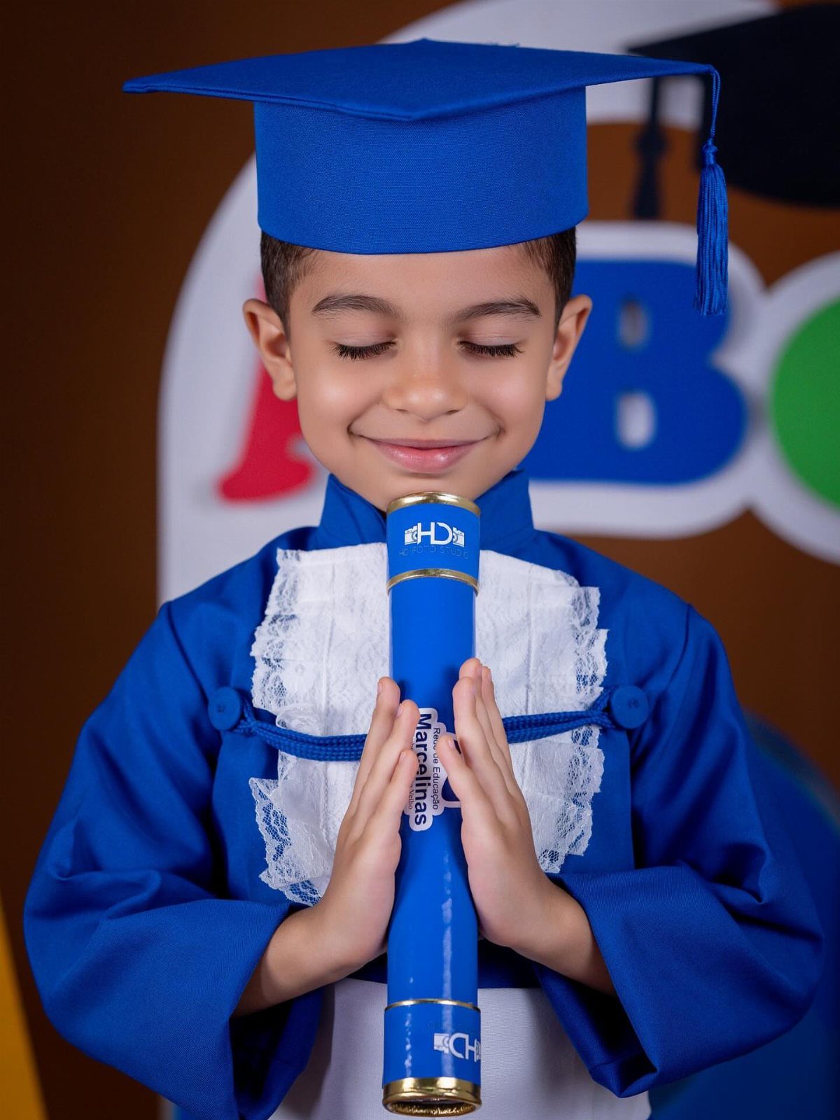 Young boy in blue graduation cap and gown holding a blue diploma tube.