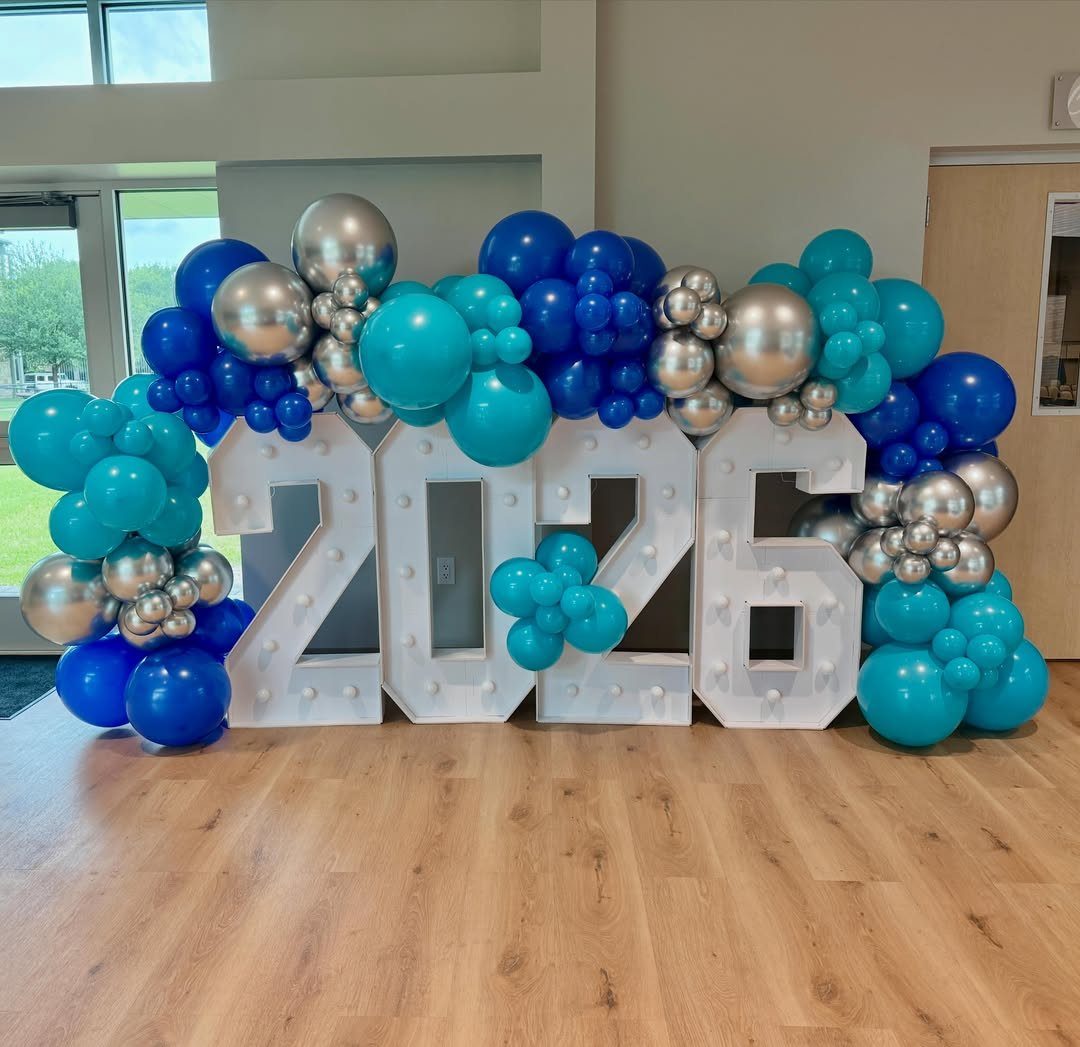 White marquee numbers 2026 surrounded by blue, teal, and silver balloons.