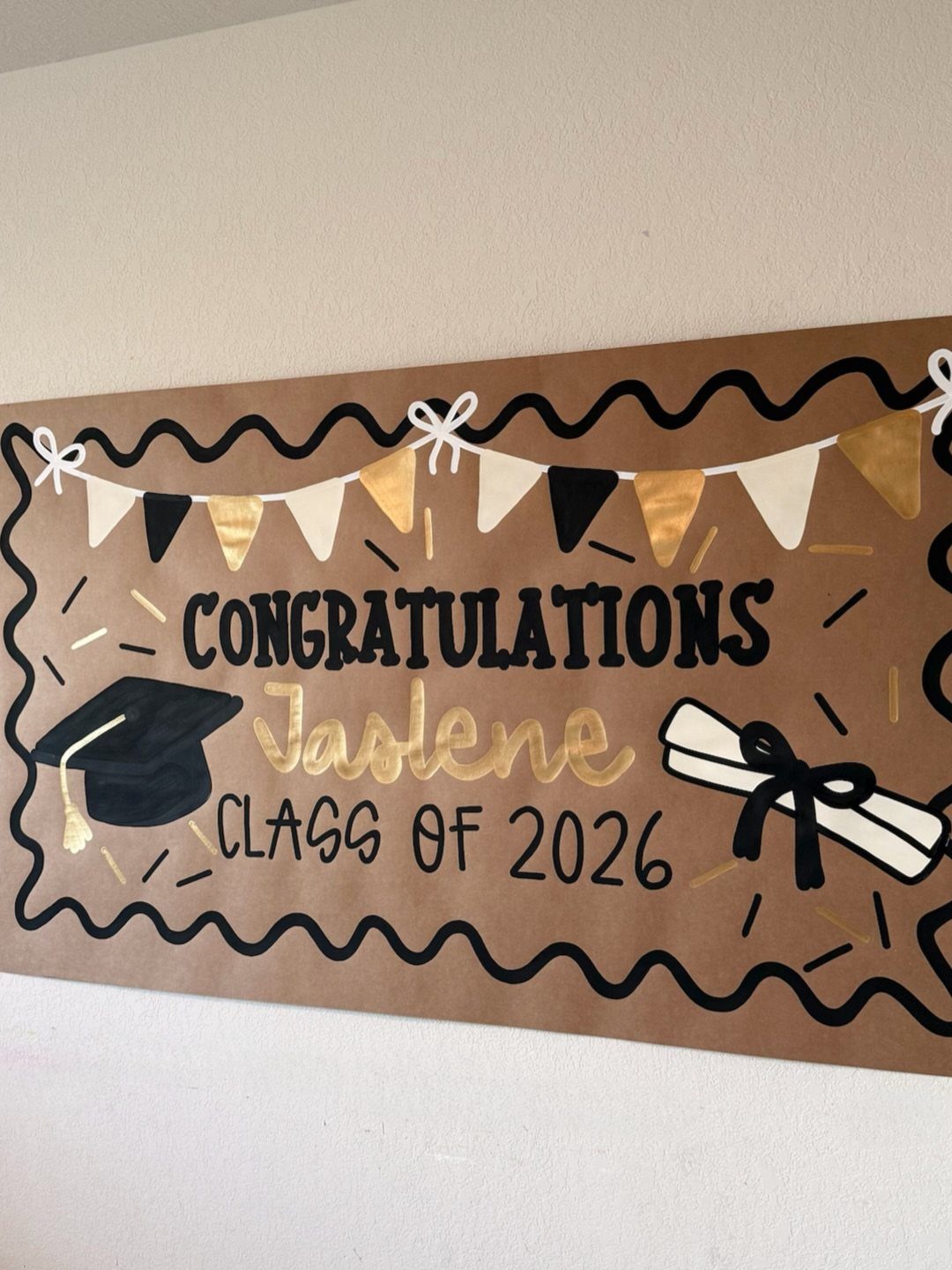 Brown paper graduation banner with gold lettering and drawings of a diploma and cap.