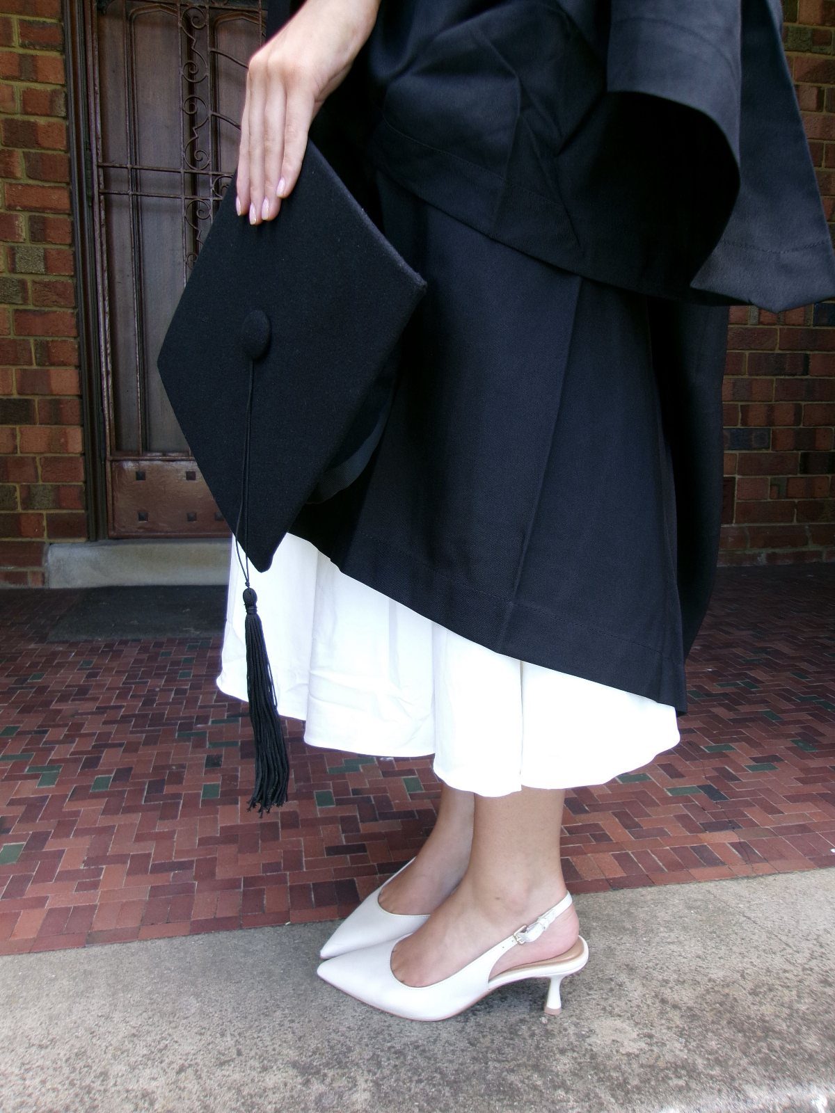 White pointed-toe slingback pumps worn with a white dress and black graduation gown.