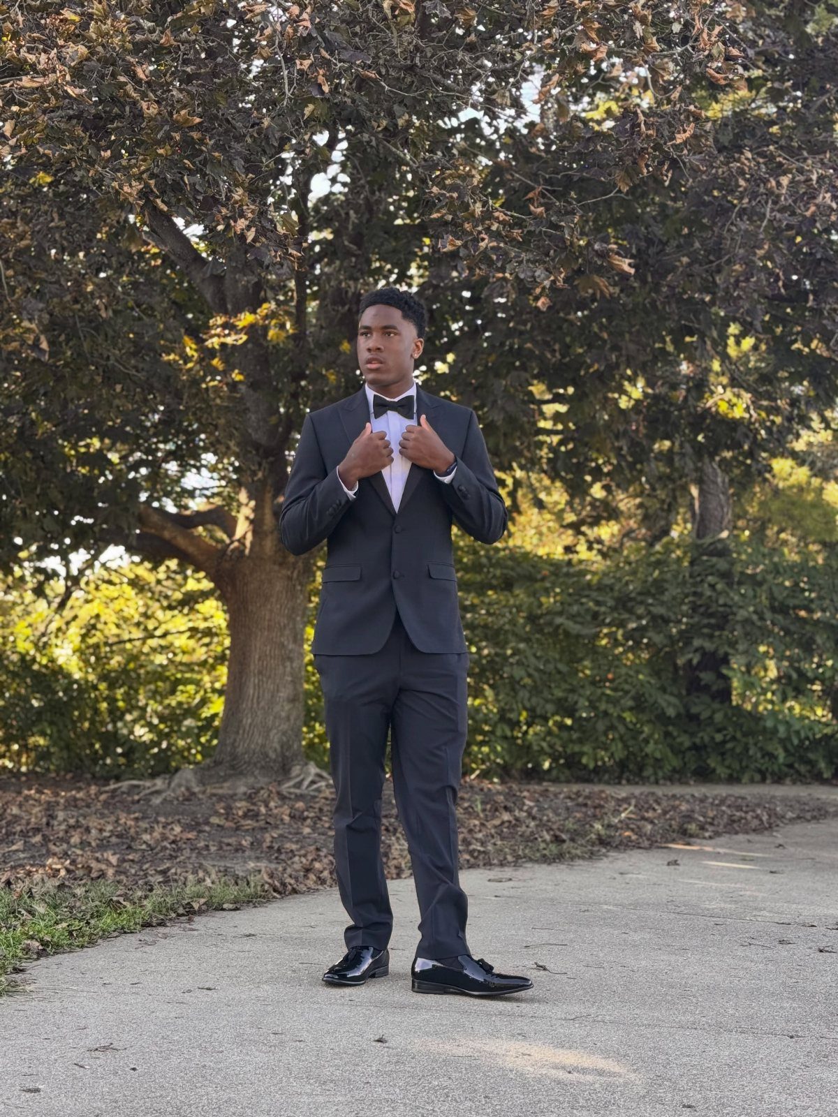 Young man in a classic black suit and bow tie posing outdoors.
