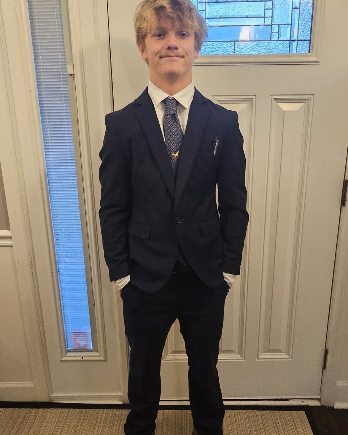 Young man wearing a navy blue suit and tie posing by a door.
