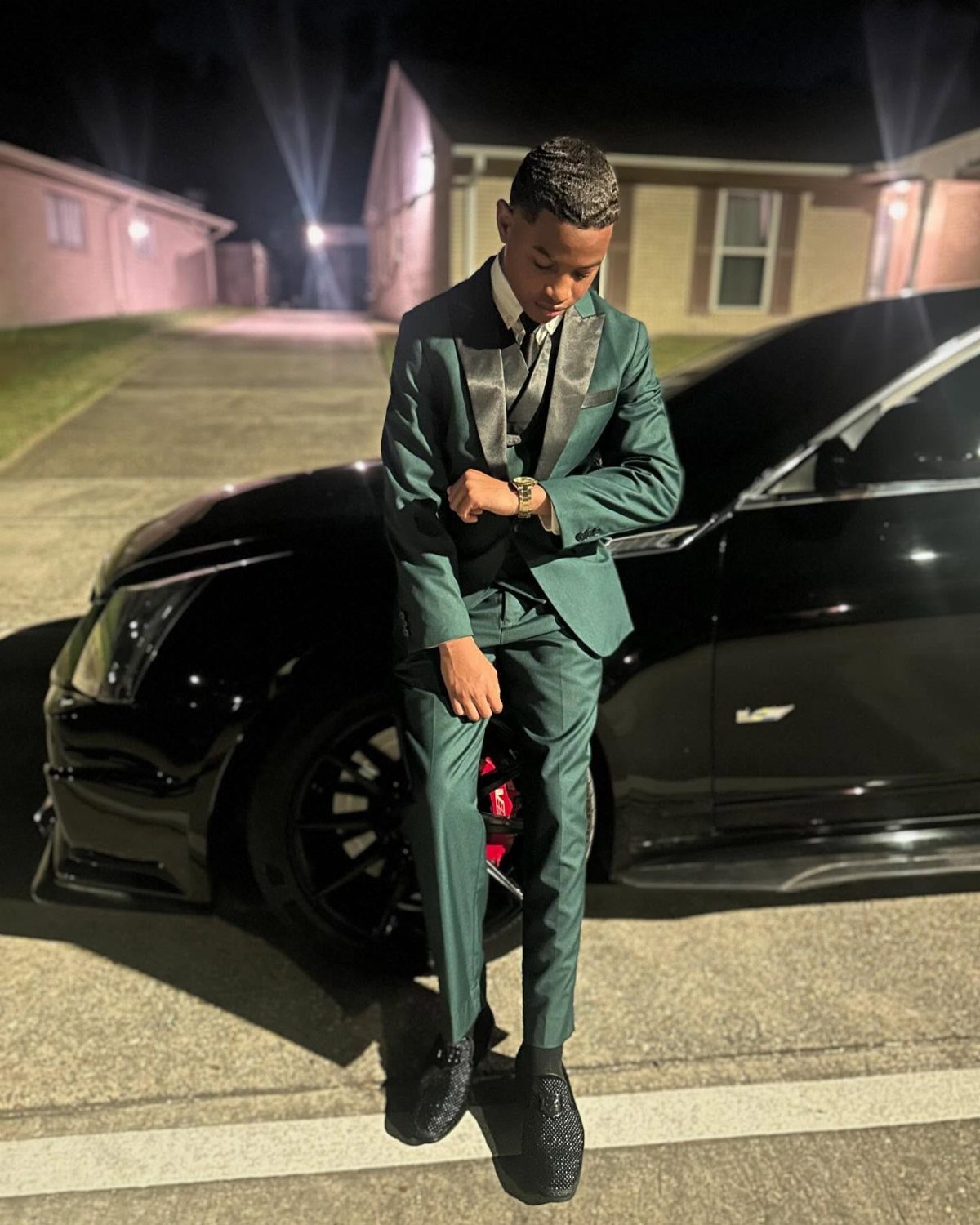 Young man in an emerald green suit posing next to a black car.