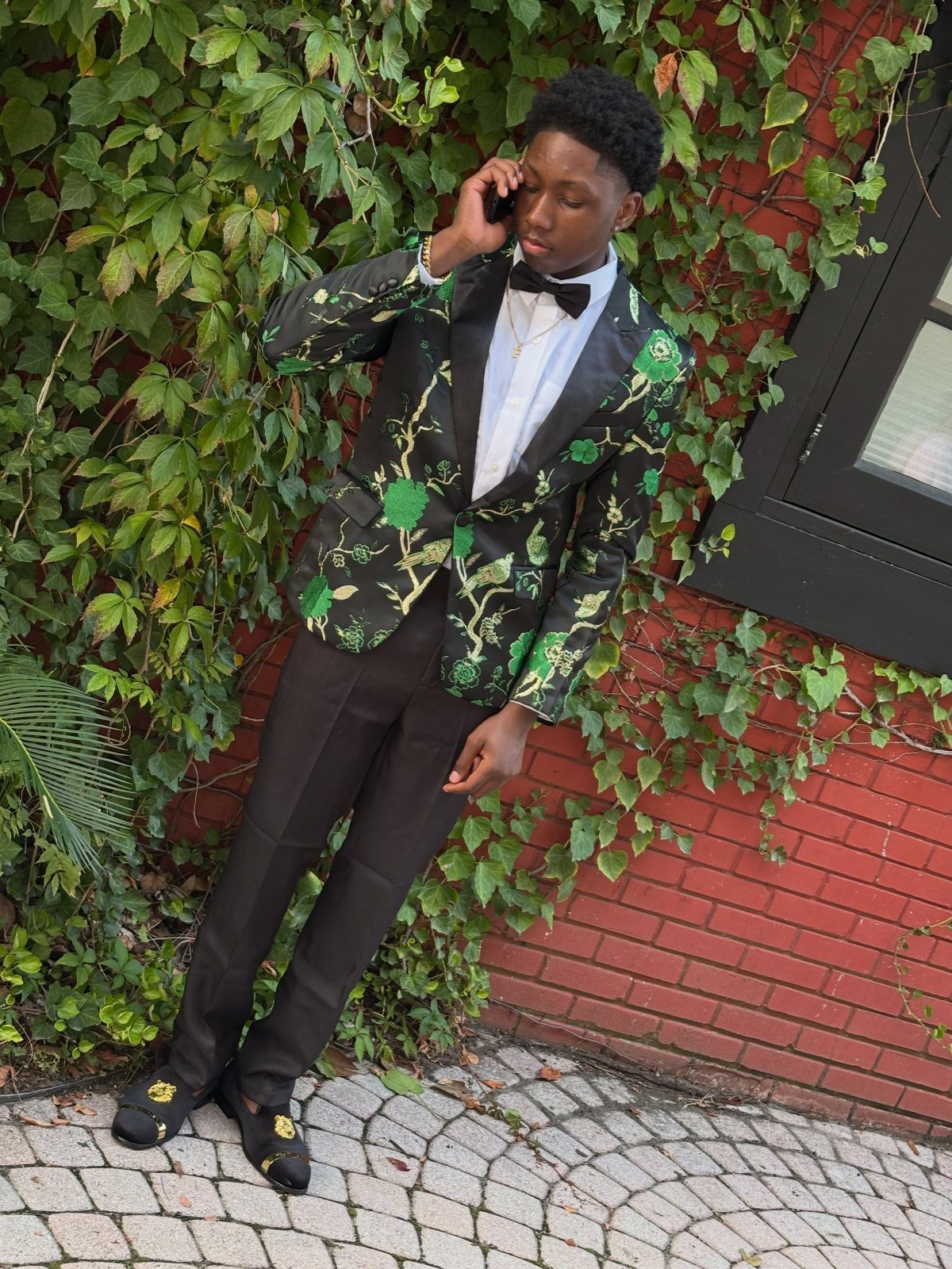 Young man in a black blazer with green floral patterns and a bow tie.