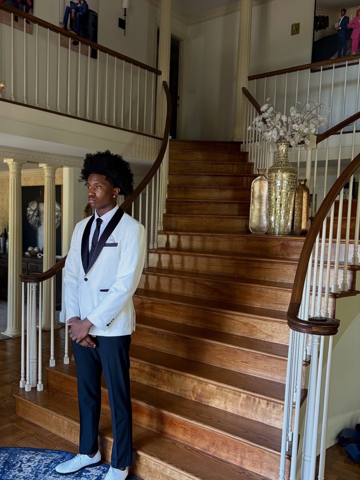 Young man in a white tuxedo jacket and black trousers standing on stairs.