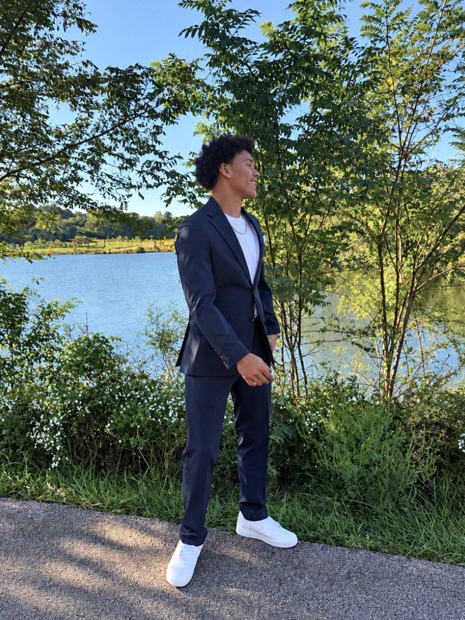 Young man in a navy blue suit and white sneakers by a lake
