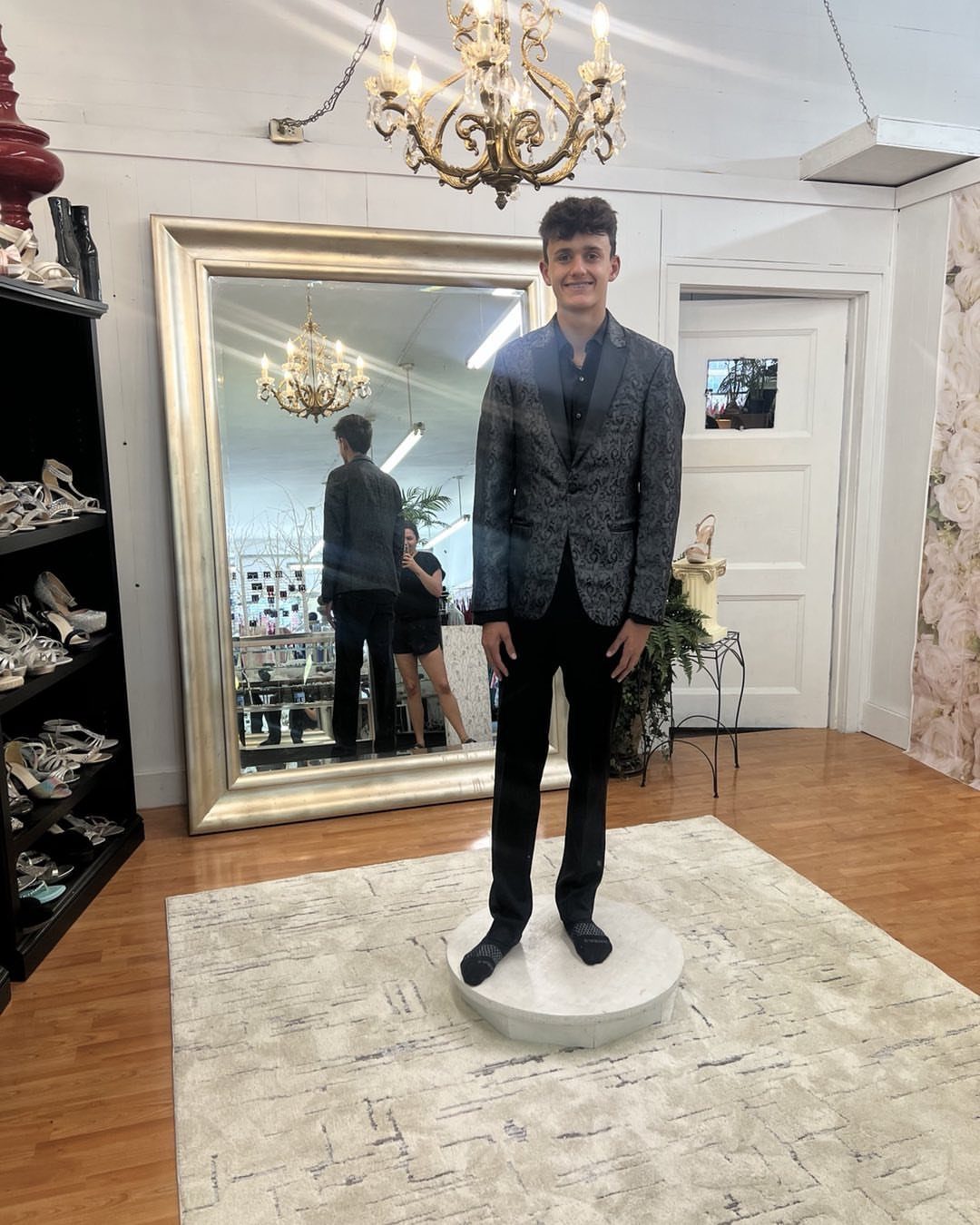 Young man wearing a dark patterned blazer and black trousers in a boutique.