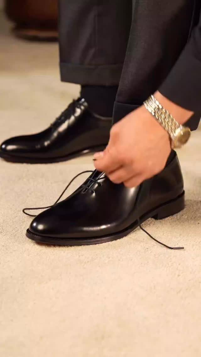 Polished black leather oxford shoes being tied by a person in formal attire.