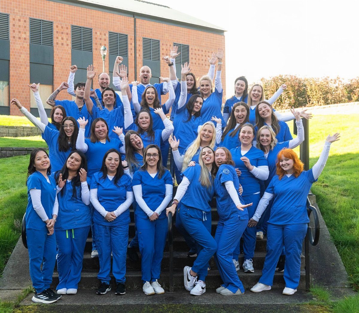 Group of nursing students in blue scrubs posing and smiling on outdoor steps.