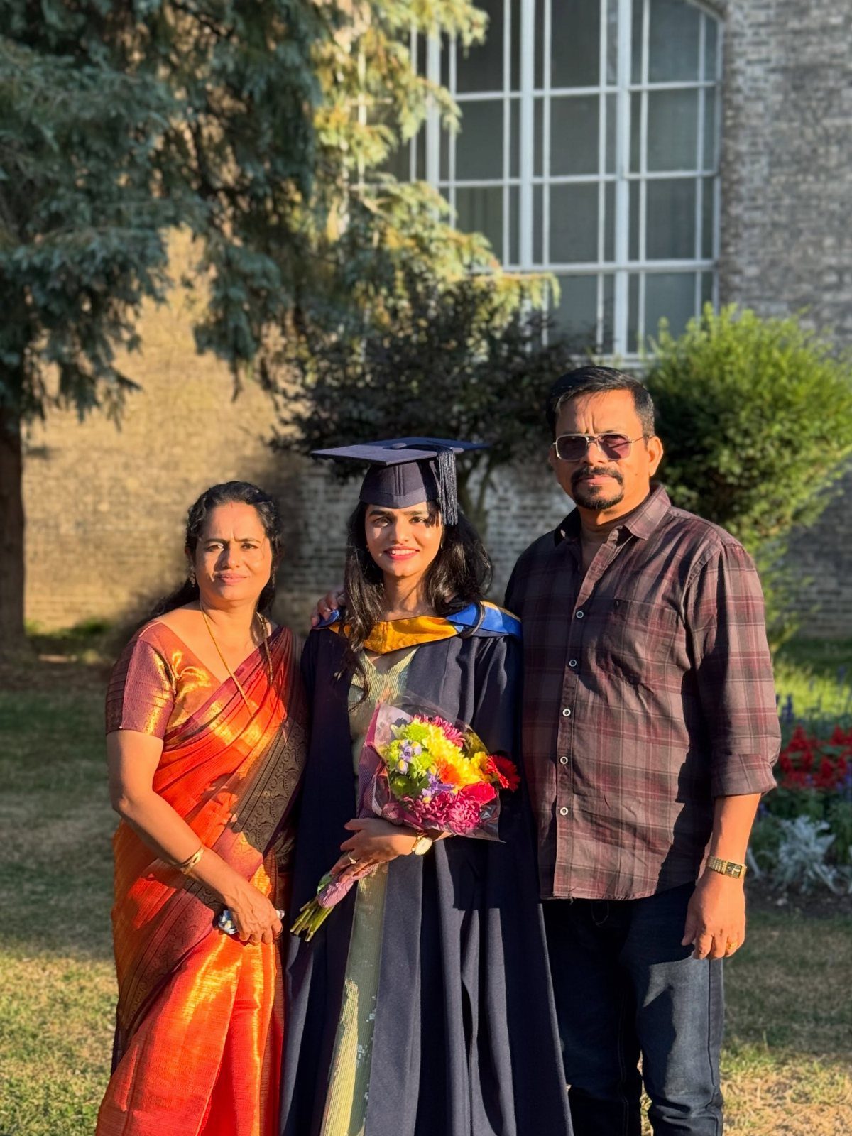Graduating woman in gown and cap posing with her parents outdoors.