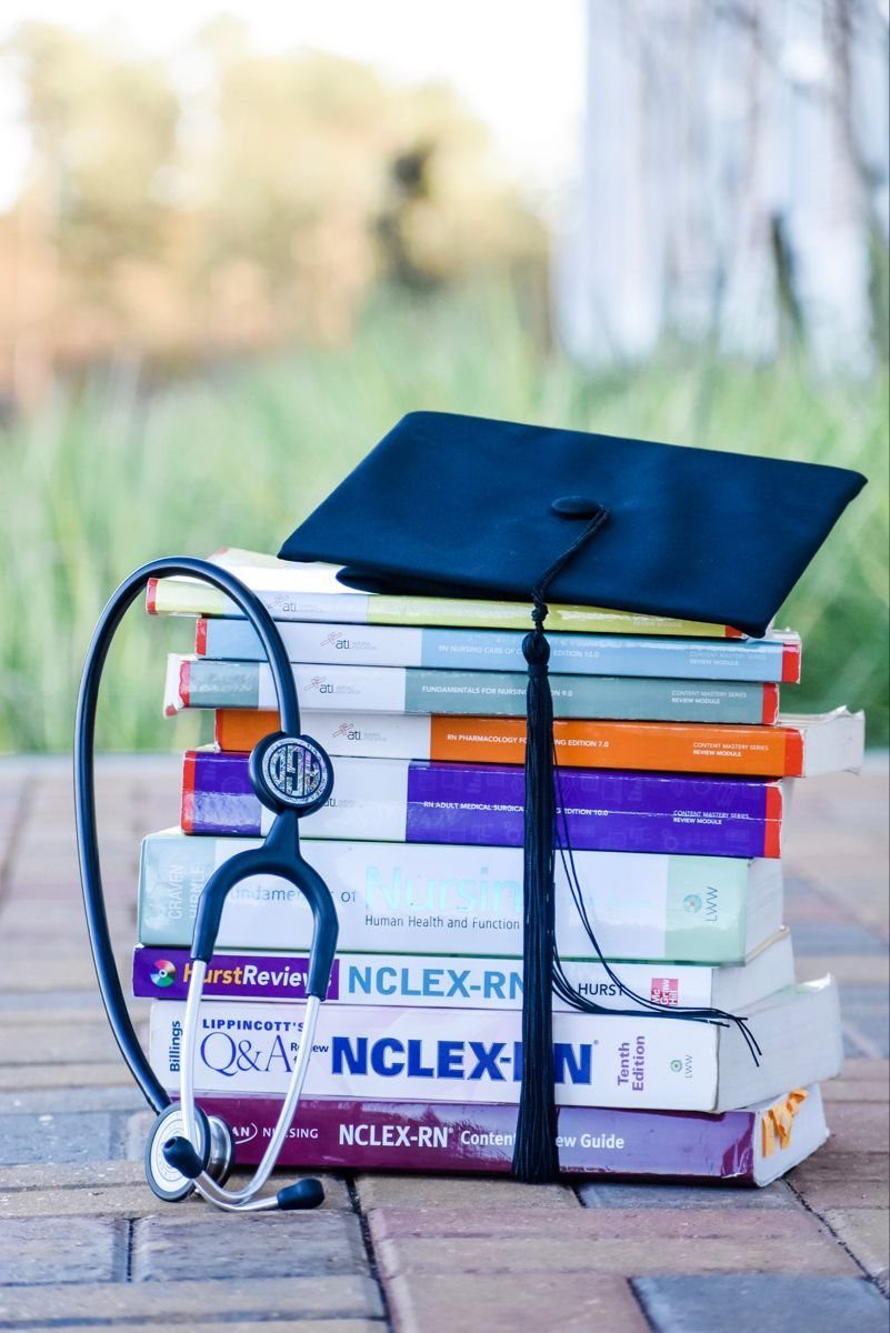 Stack of nursing textbooks topped with a graduation cap and a black stethoscope.