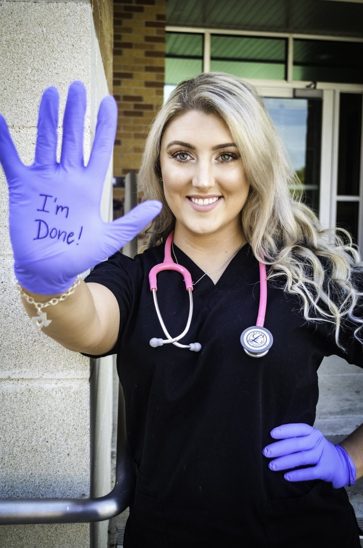 Woman in black scrubs and purple gloves holding up hand saying I'm Done!